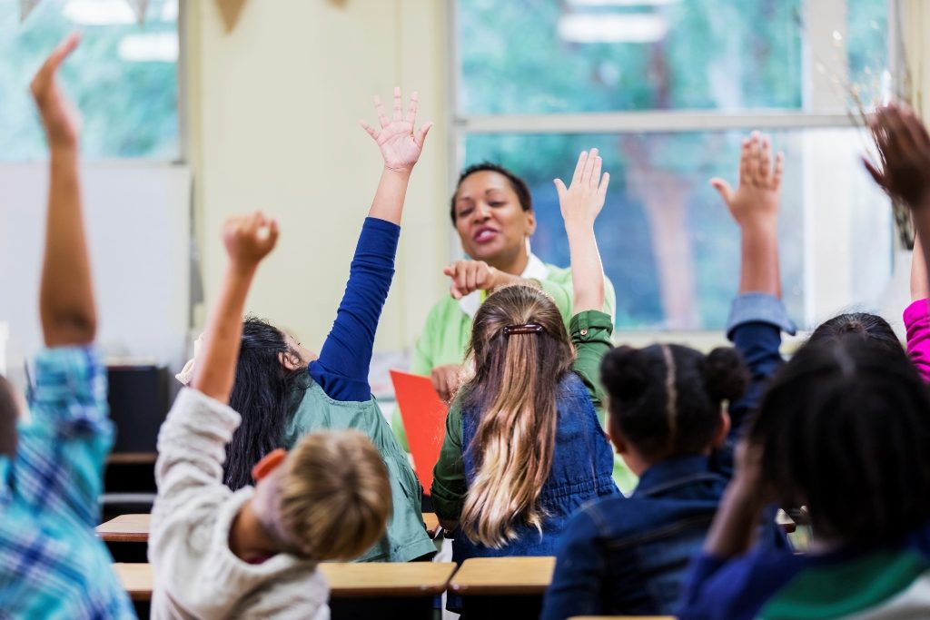 Children raising hands as their teacher choosing one of them